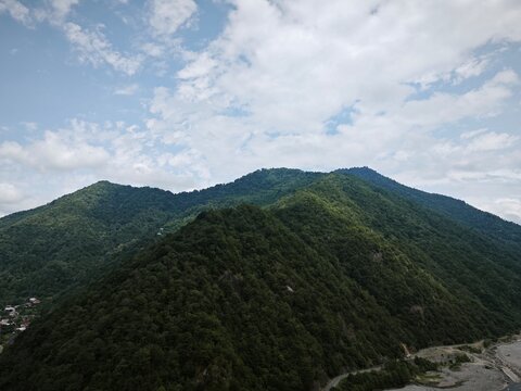 Wide landscape view of a large mountain covered in dense green forest. Rolling hills under a cloudy sky