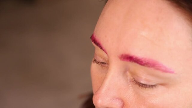 Woman receiving purple eyebrow microblading procedure by gloved hands