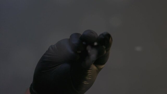 Close-up of a black gloved hand sprinkling coarse white salt from above, with falling salt crystals isolated against a dark background.
