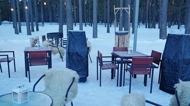 Outdoor cafe remains open in winter with snowy tables and cozy seats among trees