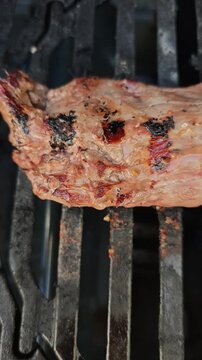 Vertical slow motion close-up of a perfectly grilled beef tenderloin steak finishing on a hot barbecue grill, browned and juicy with glowing flames and cinematic firelight in 4K