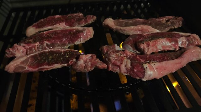 Close-up of juicy red sirloin steaks grilling on a black barbecue grate at night, illuminated only by glowing flames, cinematic firelight, 4K slow motion