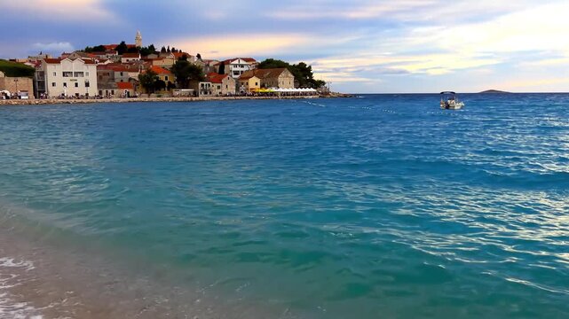 PRIMOSTEN, CROATIA - JULY 25 2017: Primosten (Capocesto) is village and municipality in Sibenik-Knin County, Croatia on Adriatic coast. Evening. People walk around city. Waves are beating on shore.
