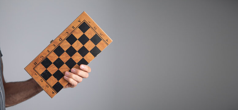Caucasian man showing chess board on grey background.