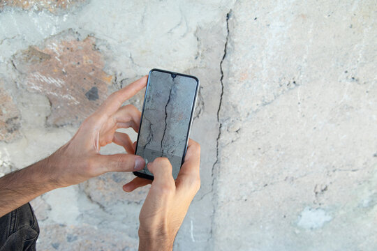 Man taking picture with a mobile phone cracked wall after earthquake.
