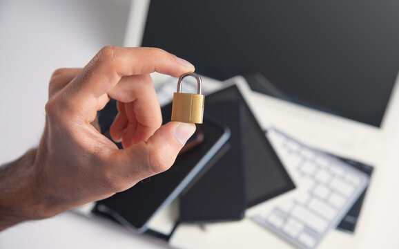 Male hand showing padlock over phones and computer keyboard. Internet and computer security