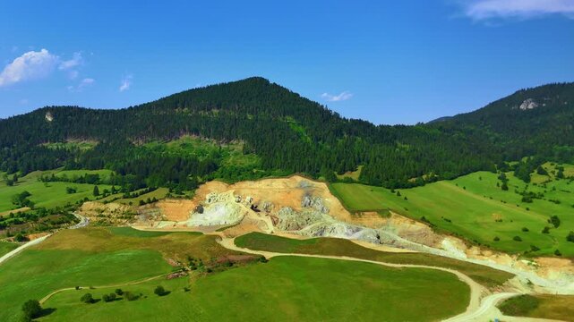 Landscape view of mountains and hills with mining activity in summer. A view shows green hills and mountains with mining work taking place under a clear sky.