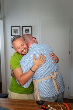Gay couple embracing each other while standing in the home kitchen