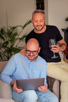 Mature same-sex partners browsing on a laptop while relaxing at home