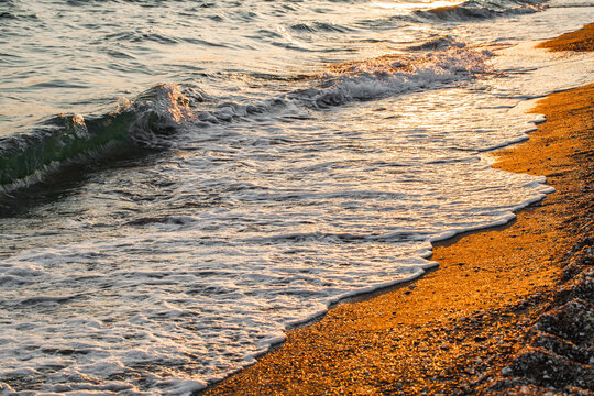 sea surf with foam on sandy beach at sunset close-up