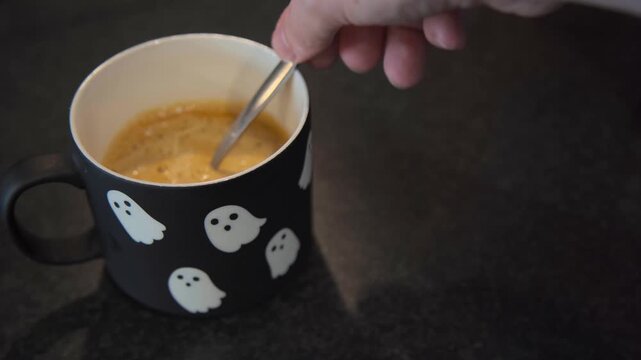 Coffee with oat milk is stirred in a Halloween ghost mug, combining seasonal lifestyle imagery with plant based and dairy free beverage content.