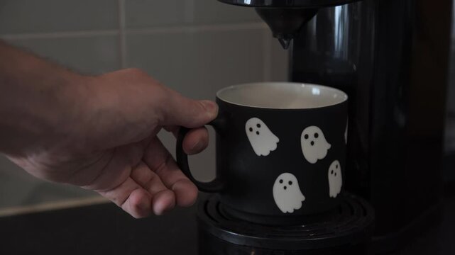 Hand places a Halloween ghost mug on a coffee machine, creating versatile seasonal lifestyle footage for workplace, home, hospitality and advertising content.