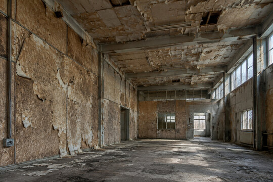 Abandoned industrial interior with peeling fiberboard walls, natural light.