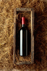 Obraz premium Bottle of red wine in an antique wooden box on a table covered with hay.