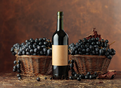 Bottle of red wine and blue grapes in old basket.