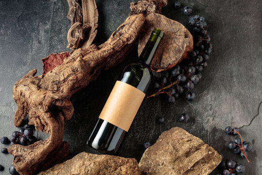 Bottle of red wine with stones, dried snags, and blue grapes.