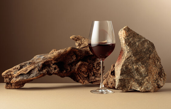 Glass of red wine with old driftwood and a piece of granite rock on a beige background.