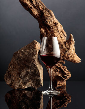 Glass of red wine with old driftwood and a piece of granite rock on a black reflective background.