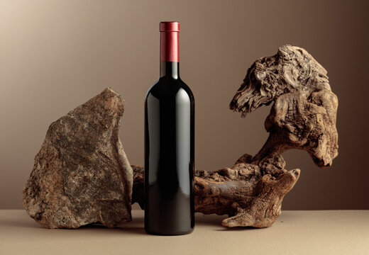 Bottle of red wine with old snag and a piece of granite rock on a beige background.