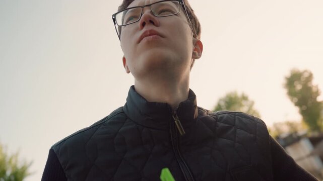 Close up shows hands holding bright green pen actively engaged in act of handwriting on paper. subject wears black quilted jacket and is positioned outdoors with soft natural light