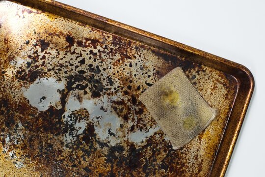 Dirty stained cookie sheet aluminum baking pan bakeware with old cleaning sponge.