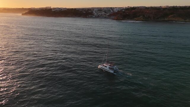 Aerial view of white sailboat on deep blue ocean water creating foamy waves. Nautical vessel sails on calm sea surface, journey towards horizon, exploring vast oceanic expanse. 