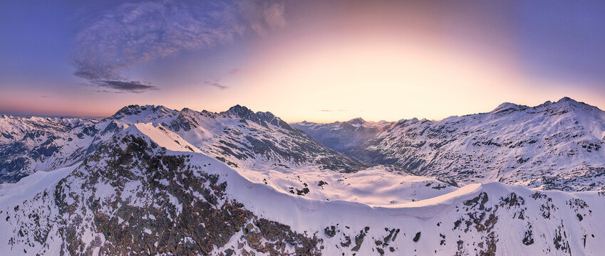 Aerial view of Vallespluga mountains covered in deep snow under a vibrant sunset sky in Lombardy, Italy.