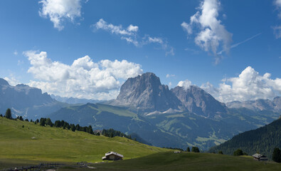Obraz premium View of beautiful landscape in the Alps with fresh green meadows and mountain tops in the background on a sunny day with blue sky and clouds in summertime. Alpe di Cisles, Seceda Ridgeline, Dolomiti ,