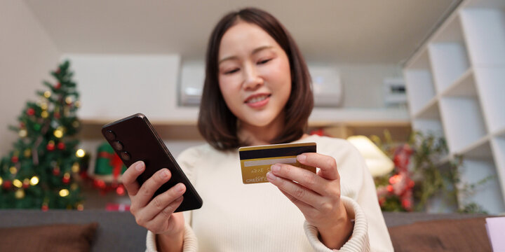 Asian woman holding credit card and smartphone for holiday online shopping at home
