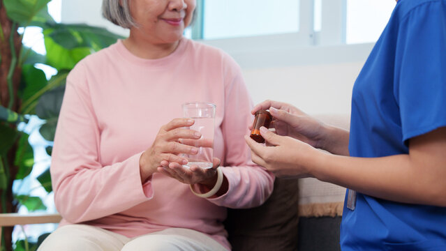 Caregiver giving pill bottle to senior woman holding water for home healthcare