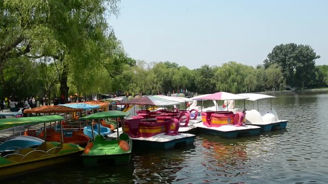 Colorful pedal boats docked by a lush green lakeside park on a sunny day