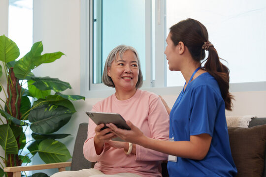 Senior woman holding tablet while consulting with Asian nurse at home