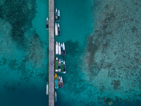 Aerial view of the Karimunjawa dockyard with various small boats moored along the concrete pier in the clear turquoise waters of the Java Sea, Karimunjawa, Jawa Tengah, Indonesia.