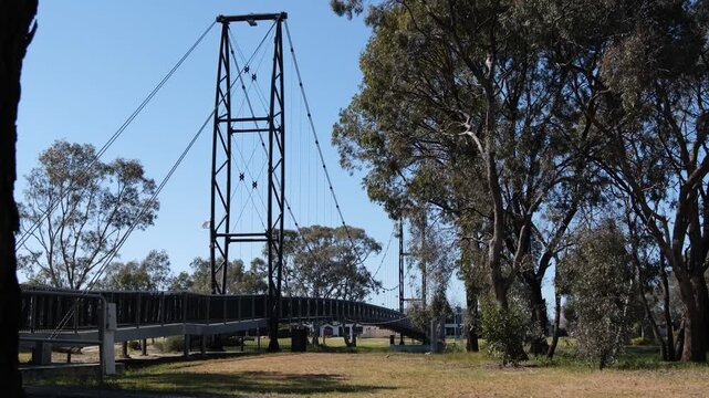 Suspension cables of the Anzac Centenary Bridge spanning the Wimmera River area in Horsham, Victoria, Australia,&nbsp;framed by native eucalyptus trees and parkland&nbsp;