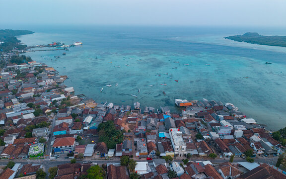 Aerial view of the coastal village of Karimunjawa with its dense rooftops, harbor filled with small boats, and turquoise bay waters in Karimunjawa, Central Java, Indonesia.