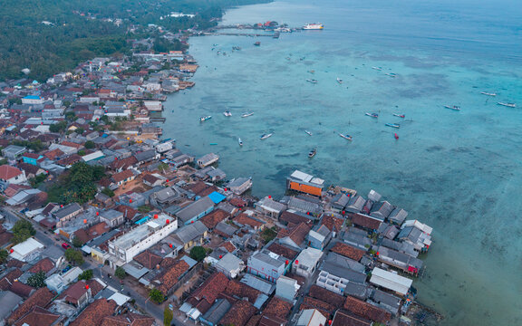 Aerial view of Karimunjawa coastal village with houses, small boats in shallow turquoise water, and lush greenery along the coastline in Karimunjawa, Central Java, Indonesia.