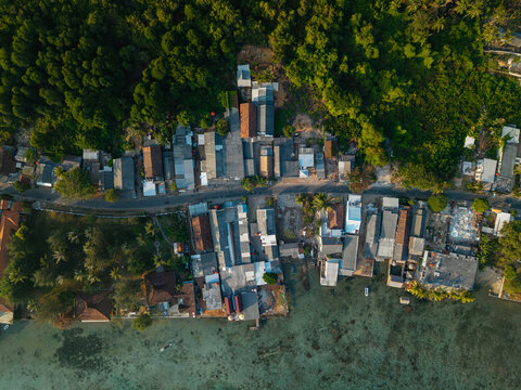 Aerial view of a coastal village with houses nestled between lush tropical trees and the clear turquoise waters of the sea in Karimunjawa, Central Java, Indonesia.