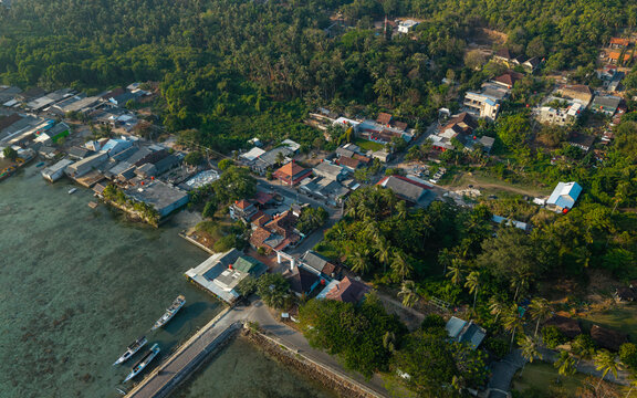 Aerial view of Karimunjawa village with traditional houses, lush tropical trees, and boats docked along the clear coastal waters in Karimunjawa, Central Java, Indonesia.