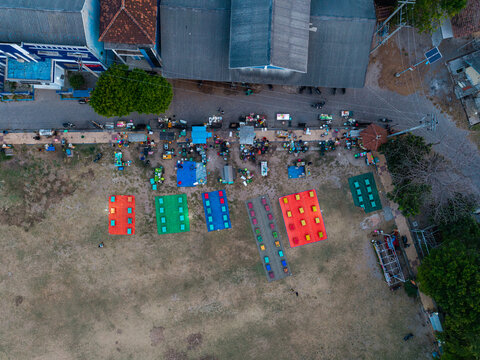 Aerial view of Karimunjawa Town Square with colorful mats and market stalls arranged on the ground, surrounded by buildings and trees in Karimunjawa, Central Java, Indonesia.