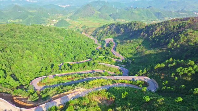 Aerial View of Winding Mountain Road Through Green Forested Hills