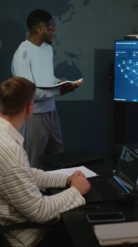Vertical shot of young adult African American specialist pointing at digital screen while Caucasian colleague codes on laptop. Clip perfect for cybersecurity, software development advertising
