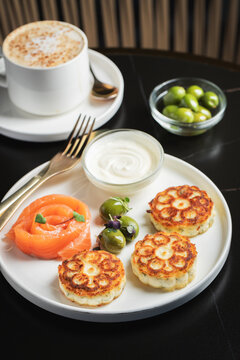 Savory Syrniki with Smoked Salmon, Olives and Sour Cream on White Plate