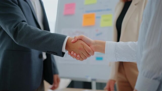 Business professionals shaking hands during a meeting with a whiteboard in the background signifying partnership and agreement
