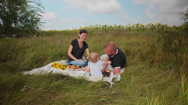 Happy parents playing with their toddler at outdoor picnic. Family having fun and enjoying time together in nature