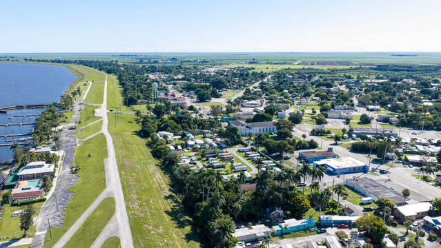 Aerial view of Pahokee along the shores of Lake Okeechobee, featuring a marina, residential areas, lush palm trees, and a clear blue sky in Pahokee, Florida, United States.