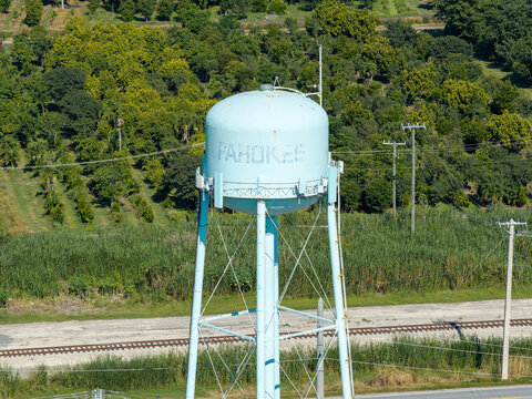 Aerial view of the Pahokee water tower standing amidst lush green vegetation and trees near a railroad track in Pahokee, Florida, United States.