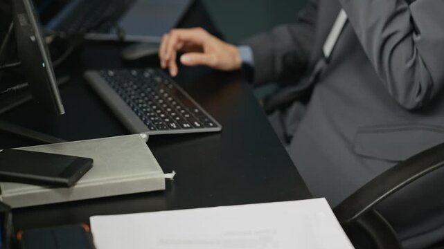 Caucasian security officer typing on computer keyboard and talking into walkie talkie at desk. Footage fits corporate cybersecurity, dispatch center, surveillance operations