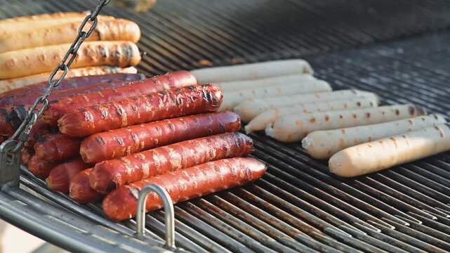 Sausages are placed on a grill with some cooked and others raw. The grilling process shows a variety of sausage colors and textures, highlighting a popular cooking method