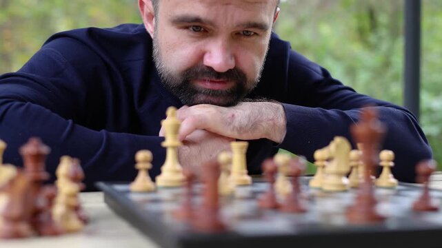 Slow motion dolly shot of a man is looking at the chessboard. His eyes are scanning the board - he is analyzing the position of the pieces on the chess field and thinking through his next move.
