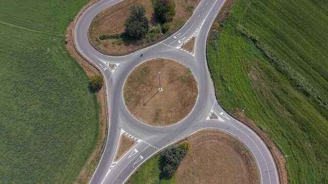 Aerial view of a rural roundabout with a cyclist and car traveling through the road junction. Useful for transportation, mobility, infrastructure, road planning and regional development storytelling.